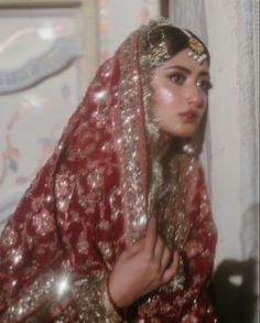 a woman in a red and gold dress with a veil on her head is looking at the camera