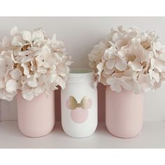 three pink vases with flowers in them on a white shelf next to a mirror