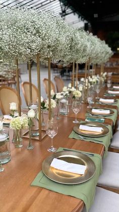 a long table set with place settings and flowers in vases on each side, along with green napkins