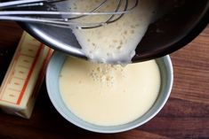 a whisk is being used to mix batter in a bowl on a wooden table