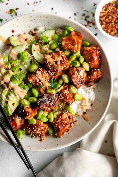 a white bowl filled with rice and meat covered in sauce next to chopsticks