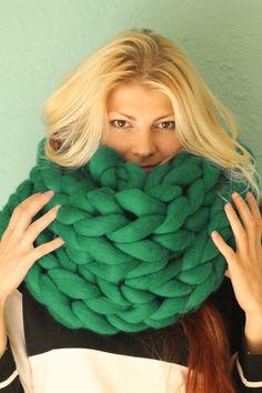 a woman with long blonde hair covering her face behind a large green knitted scarf