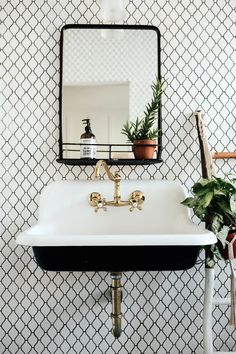 a white sink sitting under a mirror next to a potted plant on top of a table