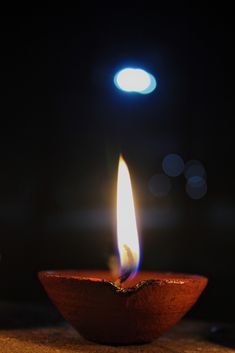 a lit candle sitting on top of a wooden table next to a light bulb in the dark