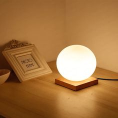 a white lamp sitting on top of a wooden table next to a bowl and framed photograph