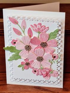 a card with pink flowers on it and green leaves in the middle, sitting on a wooden table