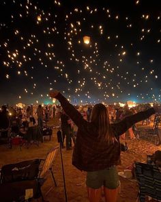 a woman standing in front of a sky full of balloons at night with her arms up