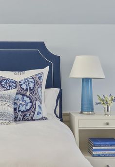 a bed with blue headboard and pillows on it next to a night stand filled with books