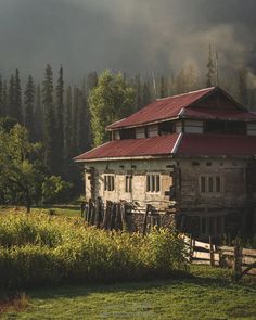 an old wooden house in the middle of a field with mountains in the back ground