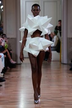 a model walks down the runway in a cutout dress with white paper on it