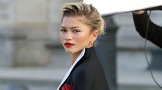 a woman with blonde hair wearing a black blazer and red lipstick holding a white umbrella