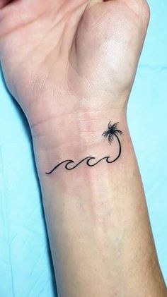 a small palm tree tattoo on the left wrist is shown in black ink, with an ocean wave behind it