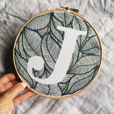 a hand embroidered monogram with the letter j surrounded by leaves on a white sheet