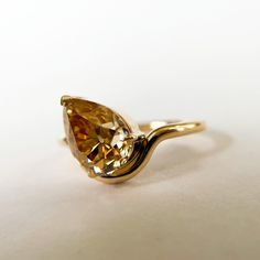 a gold ring with a pear shaped yellow diamond on it's shants, sitting on a white surface