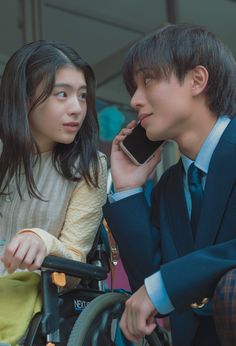 a man in a suit talking on a cell phone next to a woman in a wheelchair