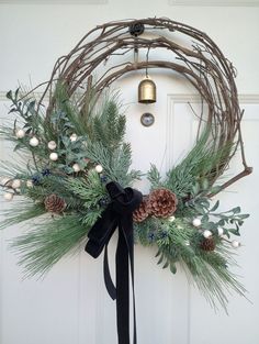 a wreath with pine cones and evergreens hanging on a door