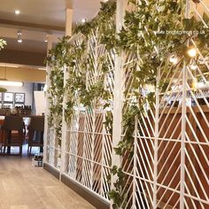 the interior of a restaurant with wooden tables and chairs covered in ivy vines, next to a white iron fence