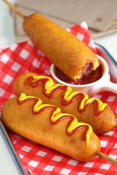 two hotdogs with ketchup and mustard on a red and white checkered tray