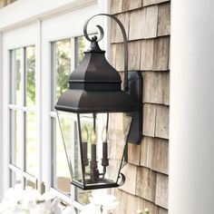 a black lantern on the side of a house next to white flowers and a window