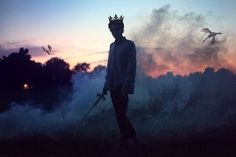 a man with a crown on his head standing in front of some clouds and birds