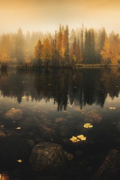 a lake surrounded by rocks and trees in the background with foggy sky above it