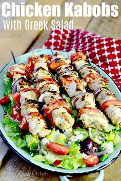 chicken kabobs with greek salad served on a white and blue plate over a wooden table