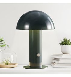 a green lamp sitting on top of a white shelf next to a potted plant