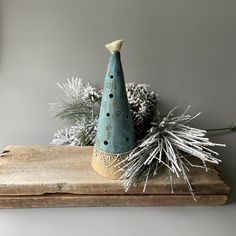 a blue ceramic christmas tree on top of a wooden shelf next to white pine cones