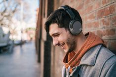 a man with headphones on looking at his cell phone in front of a brick wall