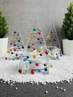 three glass christmas trees with colored balls in them on a white rug next to potted plants