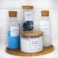 three jars filled with blue and white bath salts sitting on top of a wooden tray