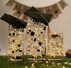 three clear glass vases with gold stars and graduation caps on them, sitting in the grass