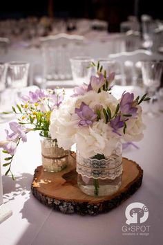 two vases with flowers are sitting on a wooden slice in front of the table