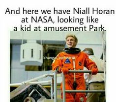 a man in an orange space suit standing next to a metal railing with the caption nasa looking like a kid at amusement park