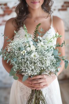 a woman holding a bouquet of white flowers and greenery in front of her face