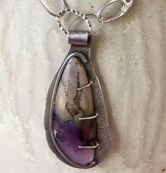 I bought this gorgeous piece of Amethyst Sage Agate a few years ago, and finally came up with a design to highlight it. The stone has gorgeous shades of purple and tan with dark variegated lines.  I tried pairing it with several combinations of stones before landing on these beautiful, faceted  Ametrine beads on one side of the design.  All of the silver chain and other findings are Sterling Silver.  I added a large clasp near the front of the necklace and included it as part of the asymmetrical Artisan Purple Amethyst Jewelry, Teardrop Amethyst Necklaces With Gemstone Accents, Oval Amethyst Natural Stones Gemstones, Oval Amethyst Necklace With Natural Stones, One Of A Kind Artisan Purple Jewelry, Artisan One-of-a-kind Purple Jewelry, Artisan Sterling Silver Purple Jewelry, Purple Artisan Sterling Silver Jewelry, Artisan Purple Sterling Silver Jewelry