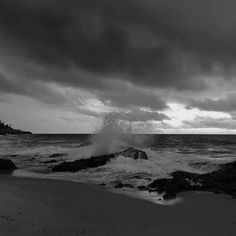 a black and white photo of waves crashing on the rocks in front of an ocean