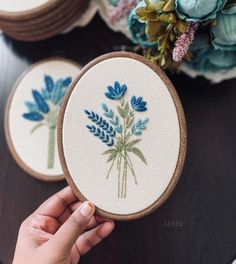 someone is holding up some cross stitch flowers on their embroidery hoop, and they are showing off the finished designs