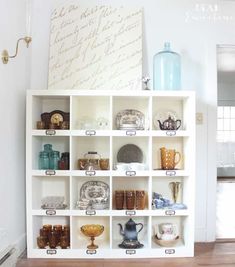 a white shelf filled with lots of glassware on top of a hard wood floor