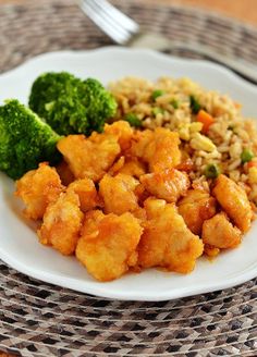 a white plate topped with chicken and rice next to broccoli on a table