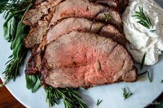 a plate with meat, mashed potatoes and fresh herbs on it next to sour cream