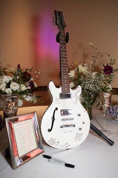 a white guitar sitting on top of a table next to a vase with flowers in it