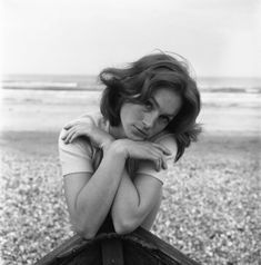 a black and white photo of a woman leaning on a boat in front of the ocean