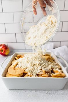 someone is sprinkling cheese on top of french fries in a baking dish with an apple in the background