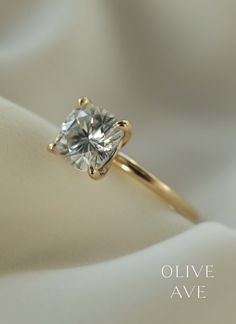 a diamond ring sitting on top of a white cloth with the words olive ave written below it