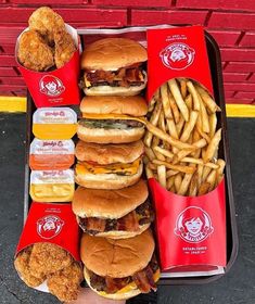 a tray filled with hamburgers and fries next to fried chicken on top of it