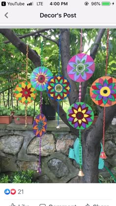 colorful wind catchers hanging from a tree in a garden with stone wall and plants