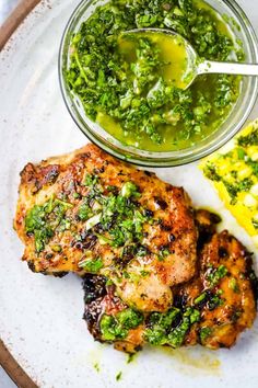 a white plate topped with chicken and broccoli next to a bowl of pesto