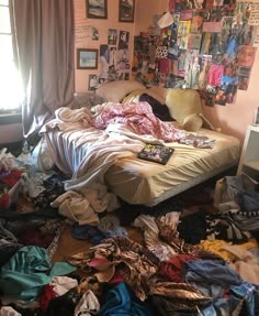 an unmade bed in a messy room with clothes scattered all over the floor and walls