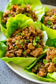 lettuce wraps filled with chicken and topped with scallions on a white plate